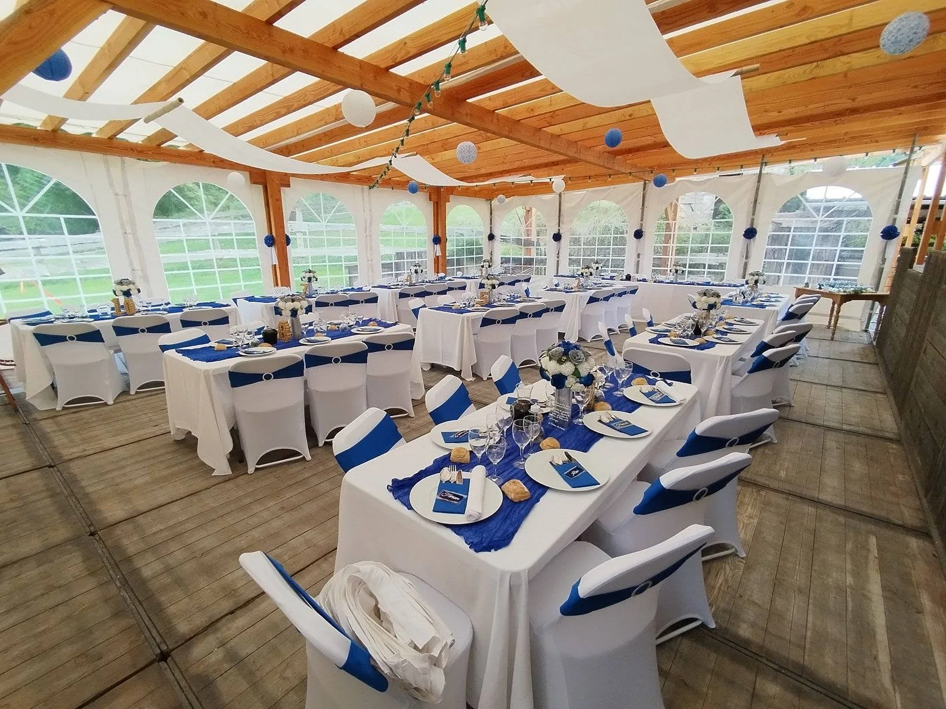 Grandes tablées dressées sous la charpente en bois, décoration en bleu roi
