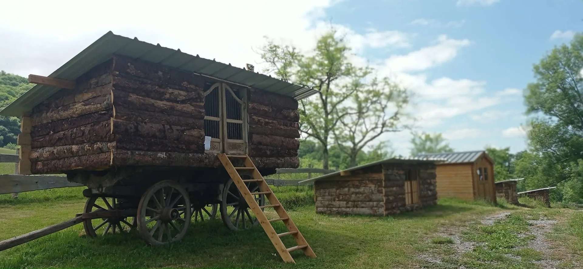 Roulotte en rondins de bois et son échelle, devant un chalet dans la prairie